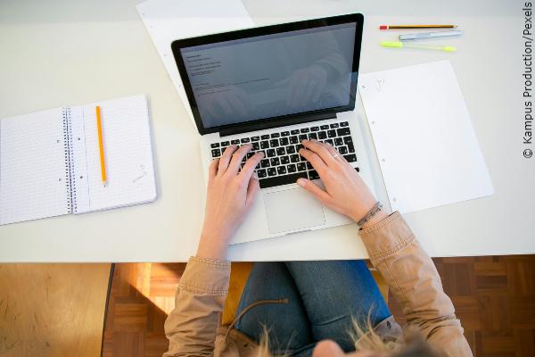 En student syns uppifrån, sitter och skriver på en laptop